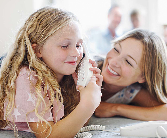 Child holding a landline phone while an adult smiles beside them